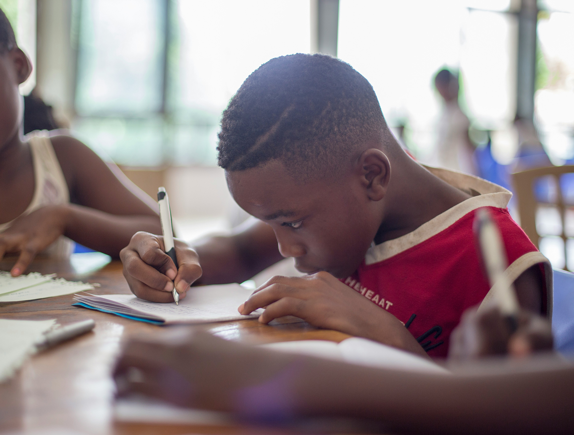 A Black elementary-school aged child is focused writing an assignment in a classroom.