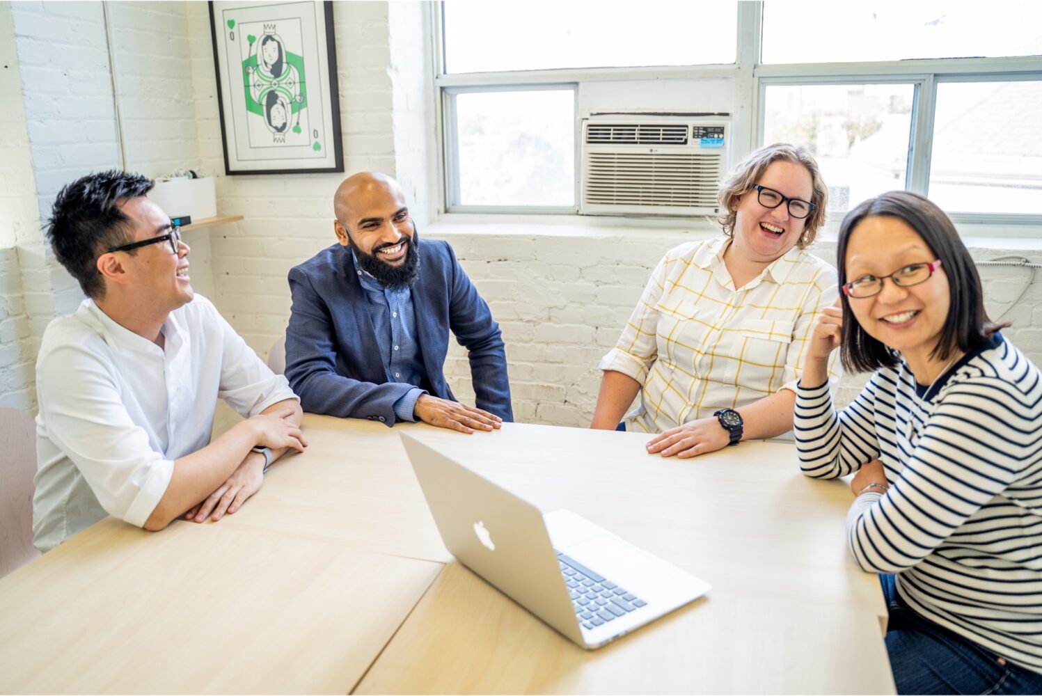 Headshot of four Grantbook employees sitting around a meeting room table, smiling and laughing