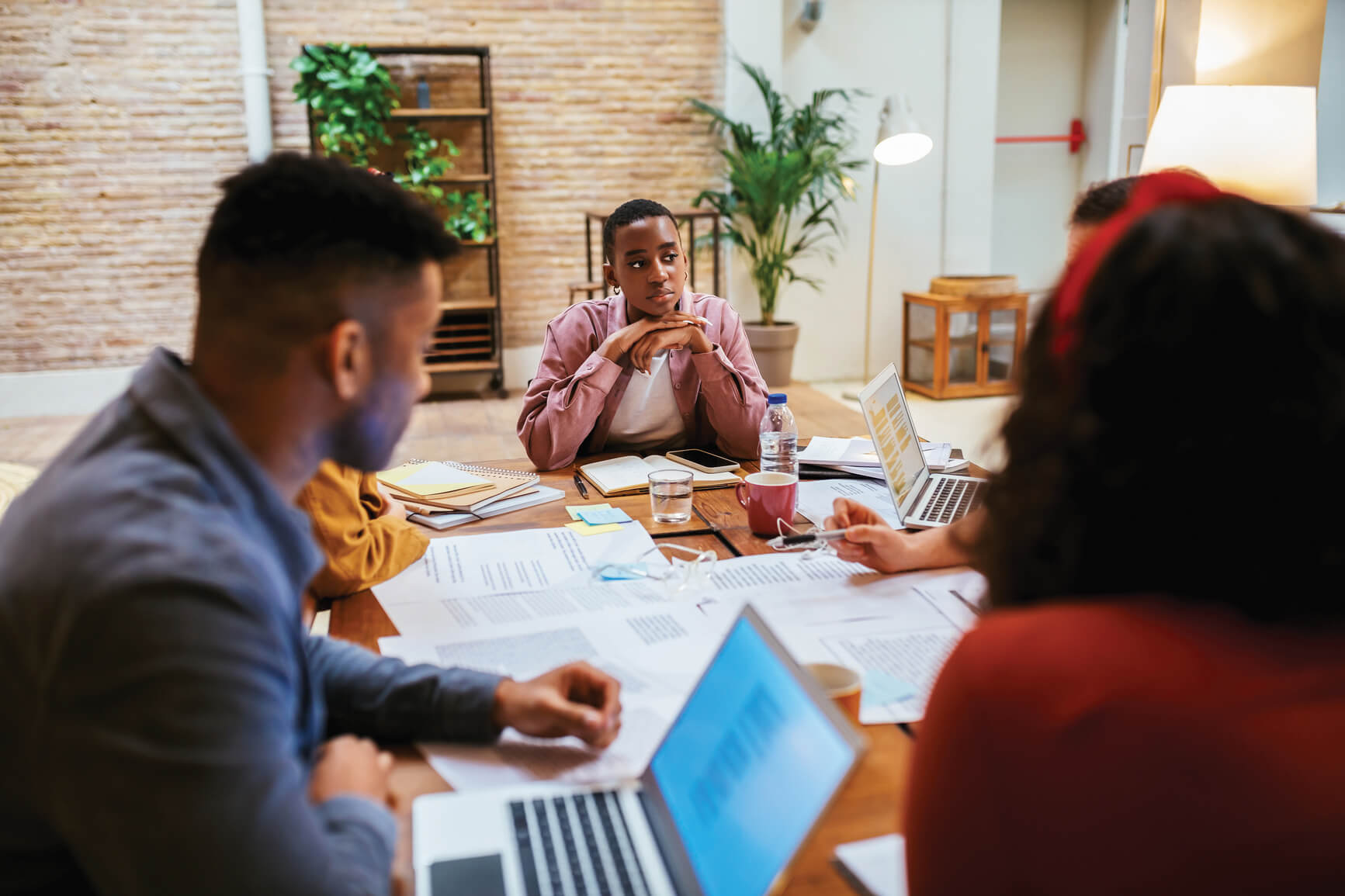 Five coworkers having a meeting. Focus on one female coworker who is listening attentively