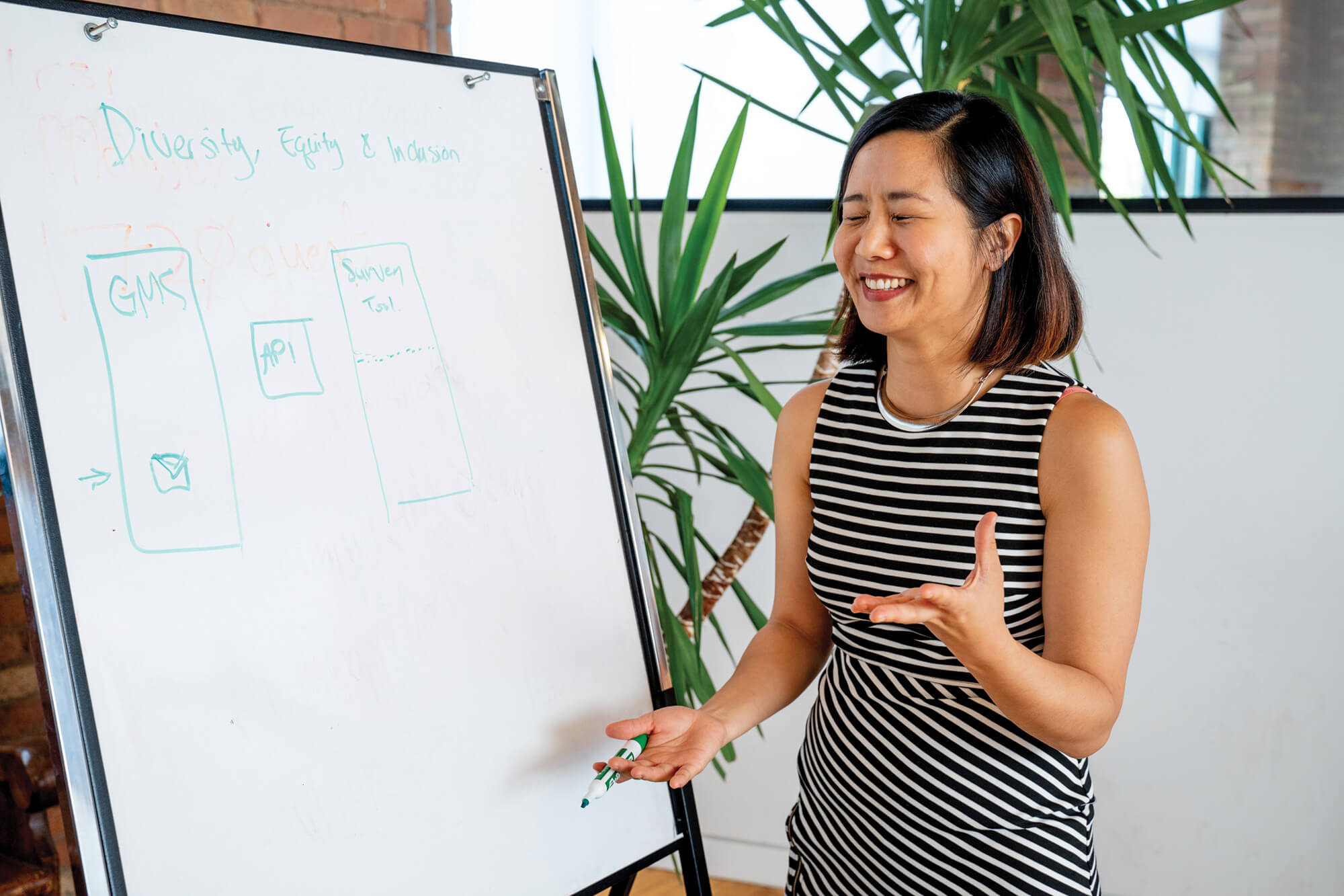 An Asian female Grantbook employee laughing, standing in front of a whiteboard, holding a marker