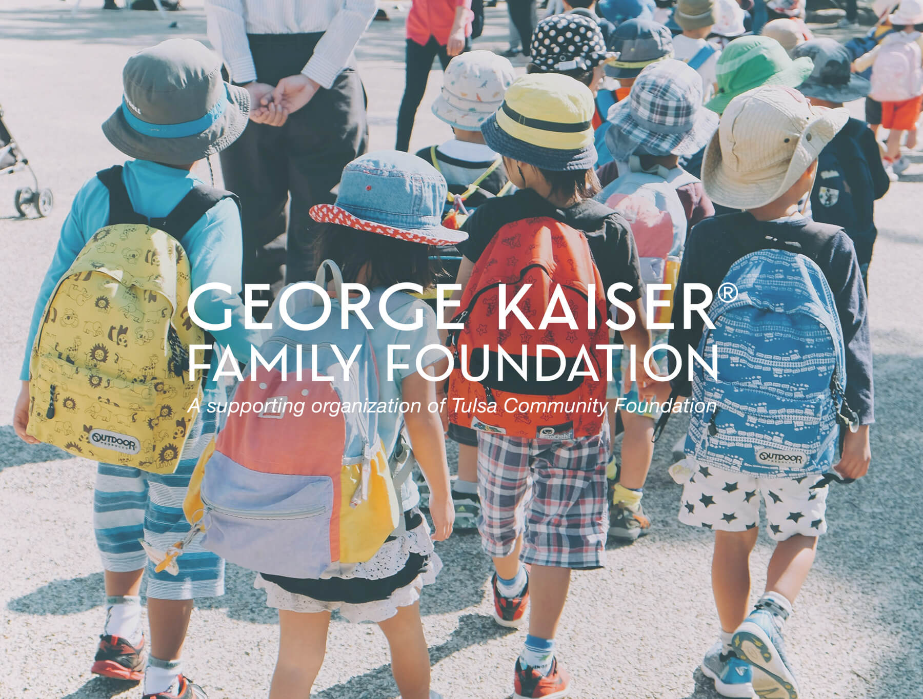 A group of young kids walking, wearing backpacks. The George Kaiser Family Foundation logo is overlaid on top of the image.