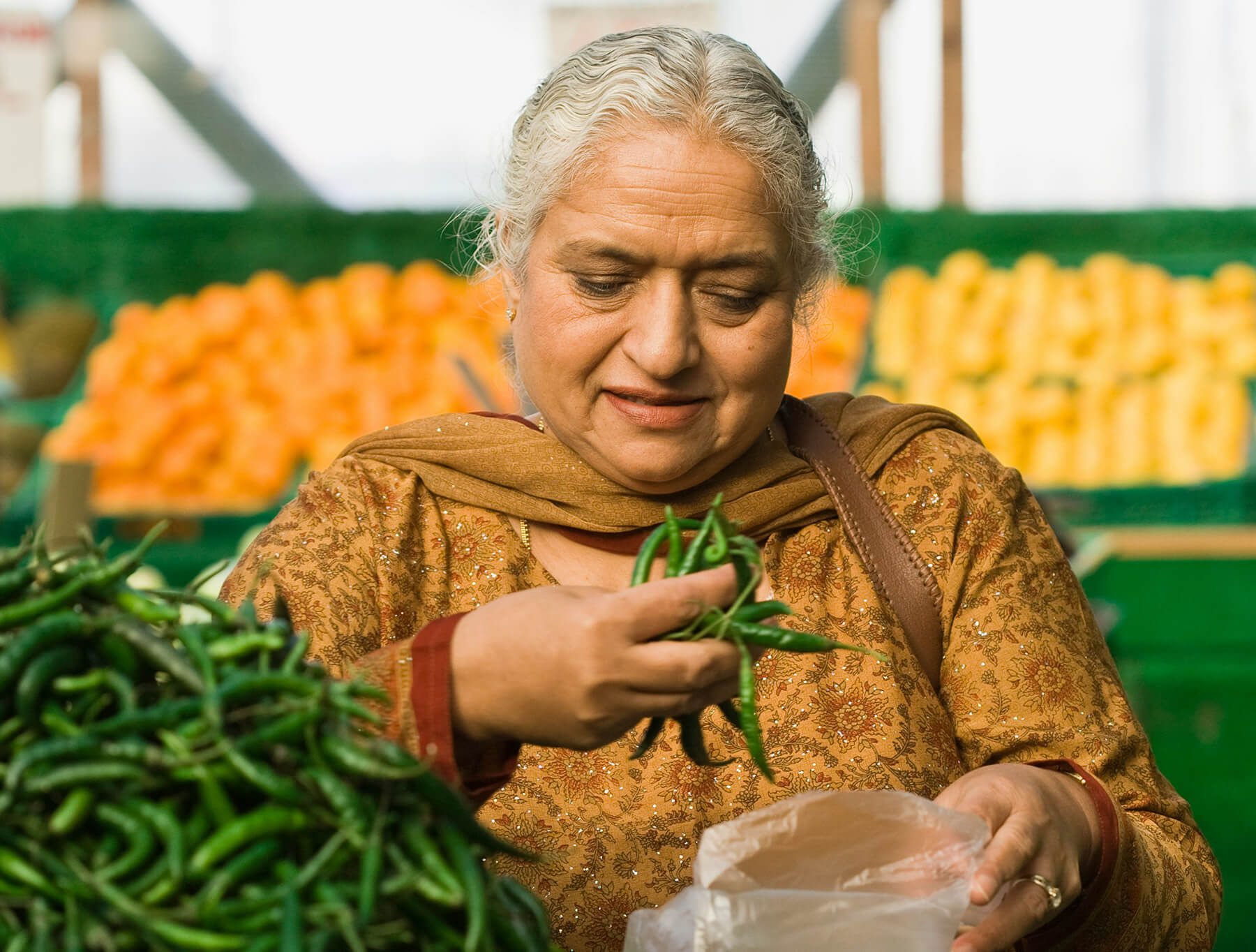 Woman at a market, filling a bag with green chilis