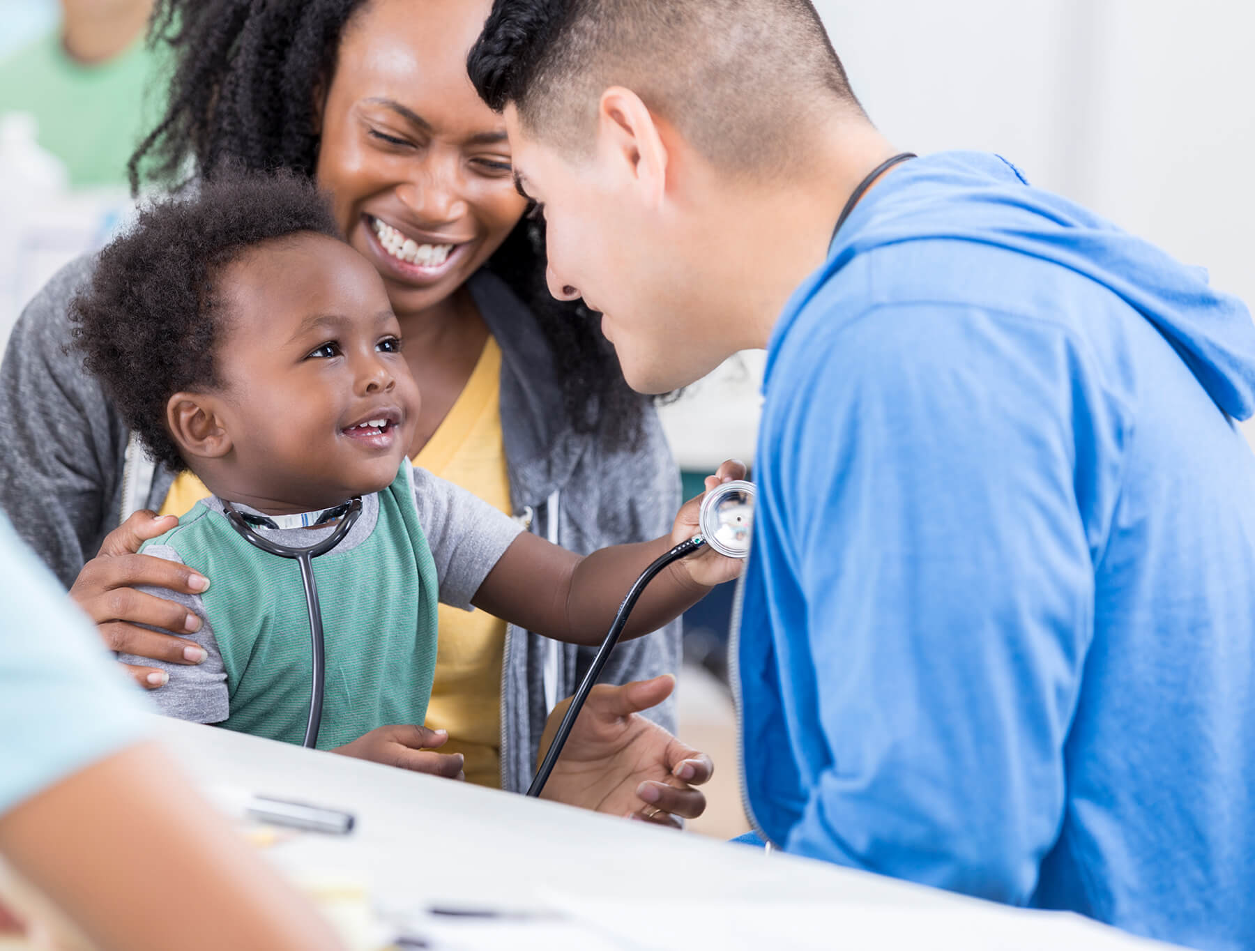 A mother holding her baby, who is holding a stethescope to a doctor's chest